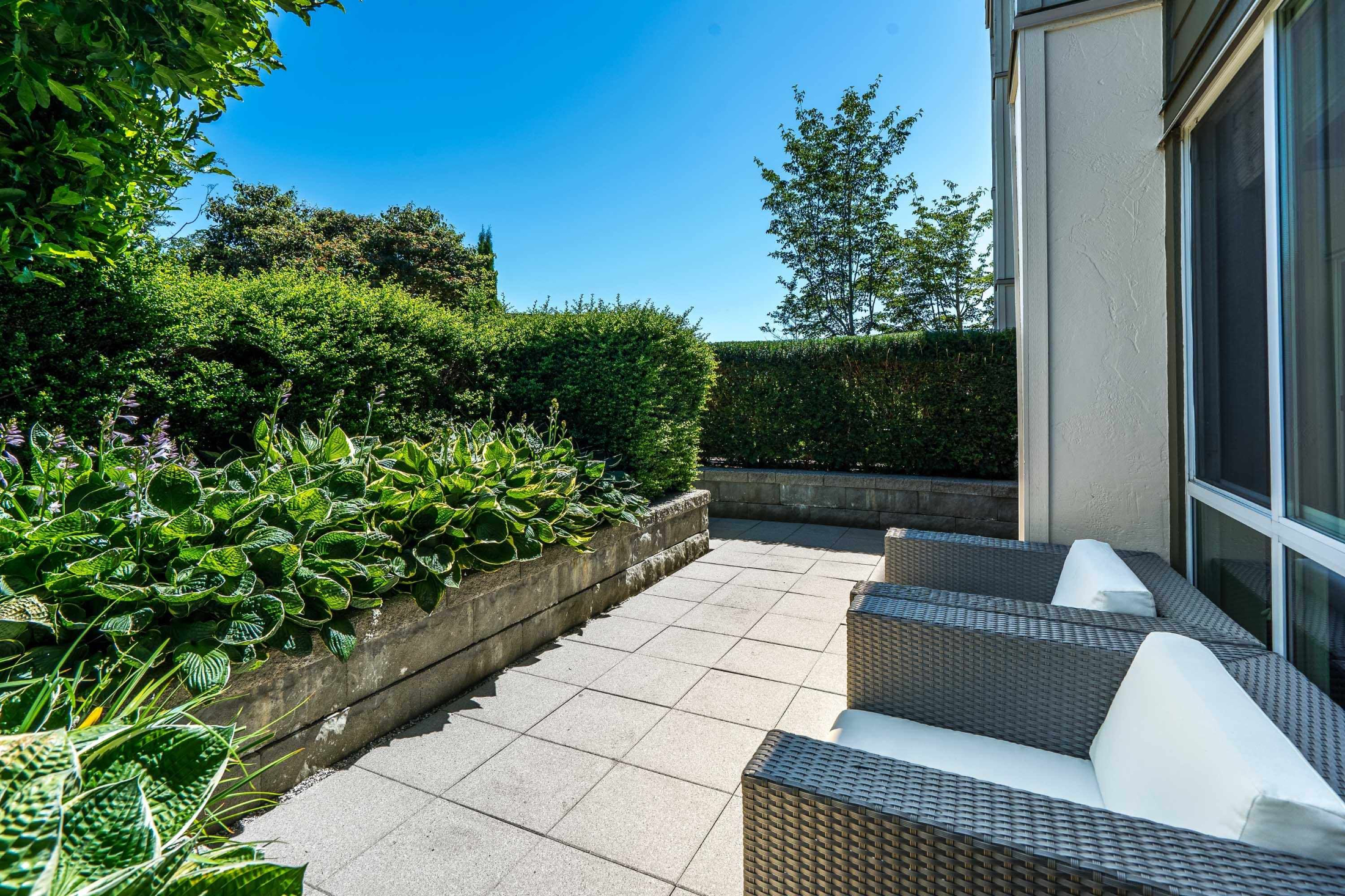 Private patio seating area with wicker chairs and landscaped greenery