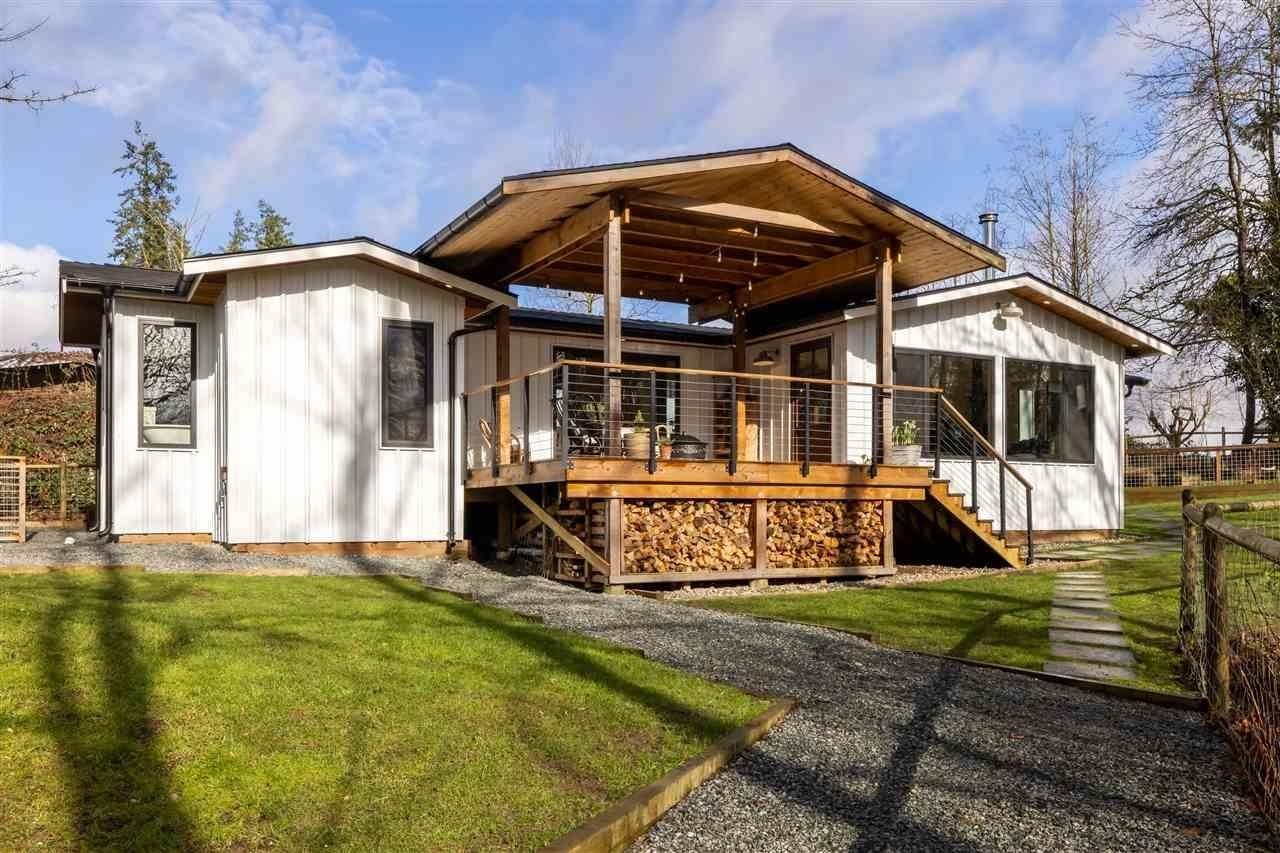 Renovated rural home with a covered wood deck and stacked firewood on a Langley hobby farm